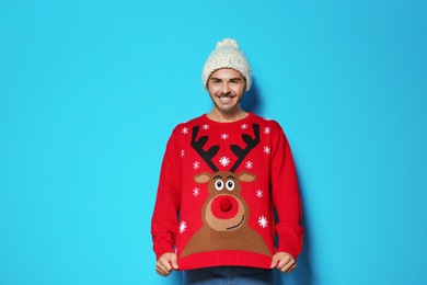 Young man in Christmas sweater and knitted hat on color background