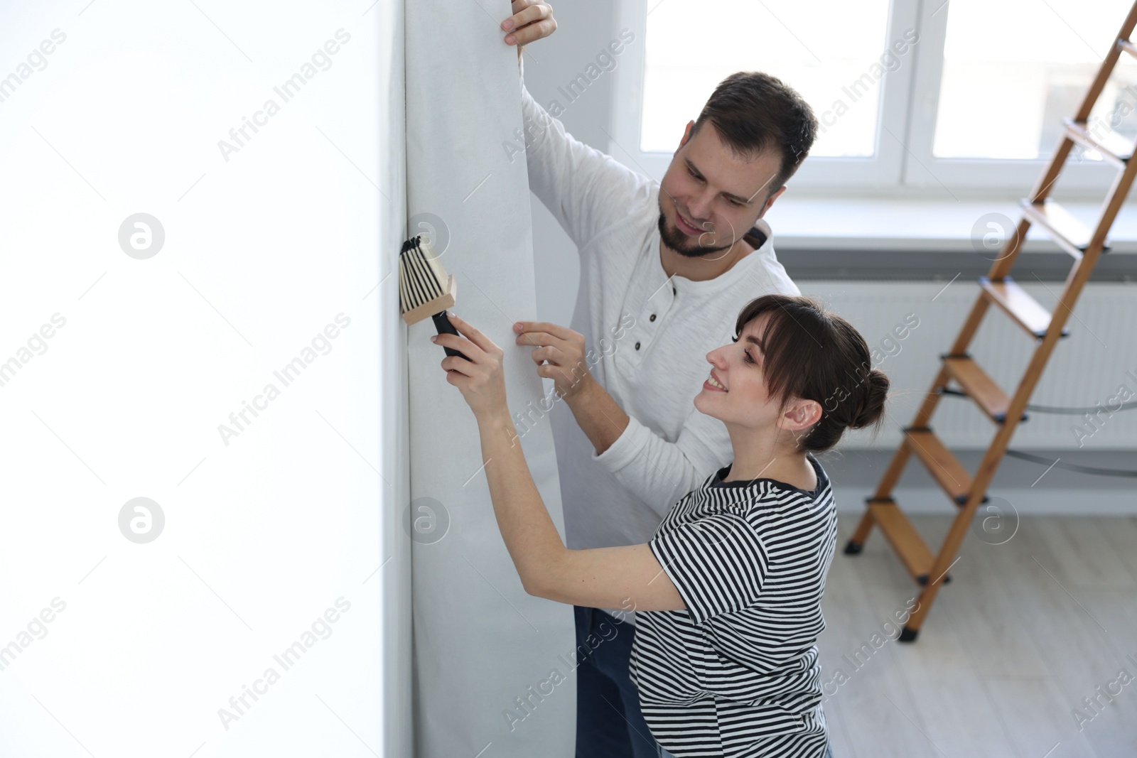 Photo of Woman and man hanging wallpaper in room