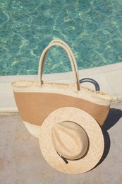 Photo of Stylish bag and hat near outdoor swimming pool on sunny day. Beach accessories