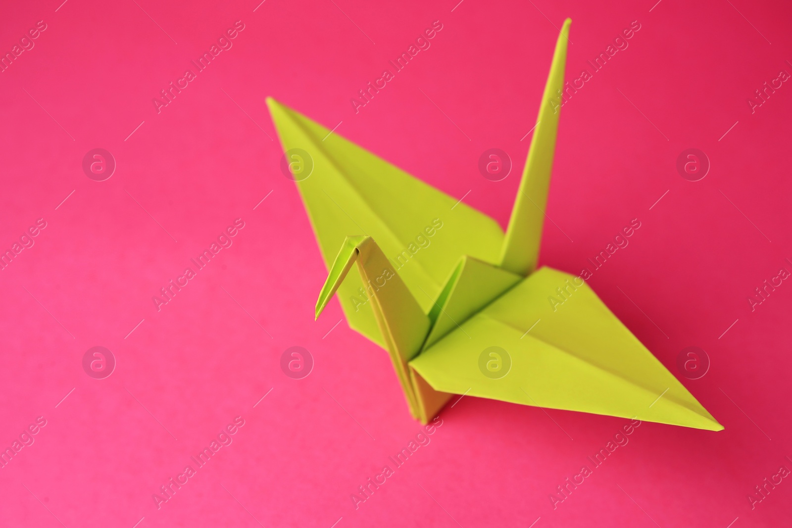 Photo of Origami art. Handmade paper crane on pink background, closeup. Space for text