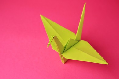 Origami art. Handmade paper crane on pink background, closeup. Space for text
