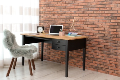 Stylish workplace interior with laptop on table near brick wall. Space for text