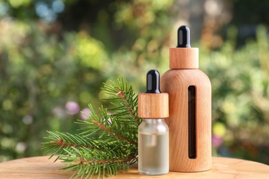 Bottles of pine essential oil and branches on wooden table against blurred background, closeup. Space for text