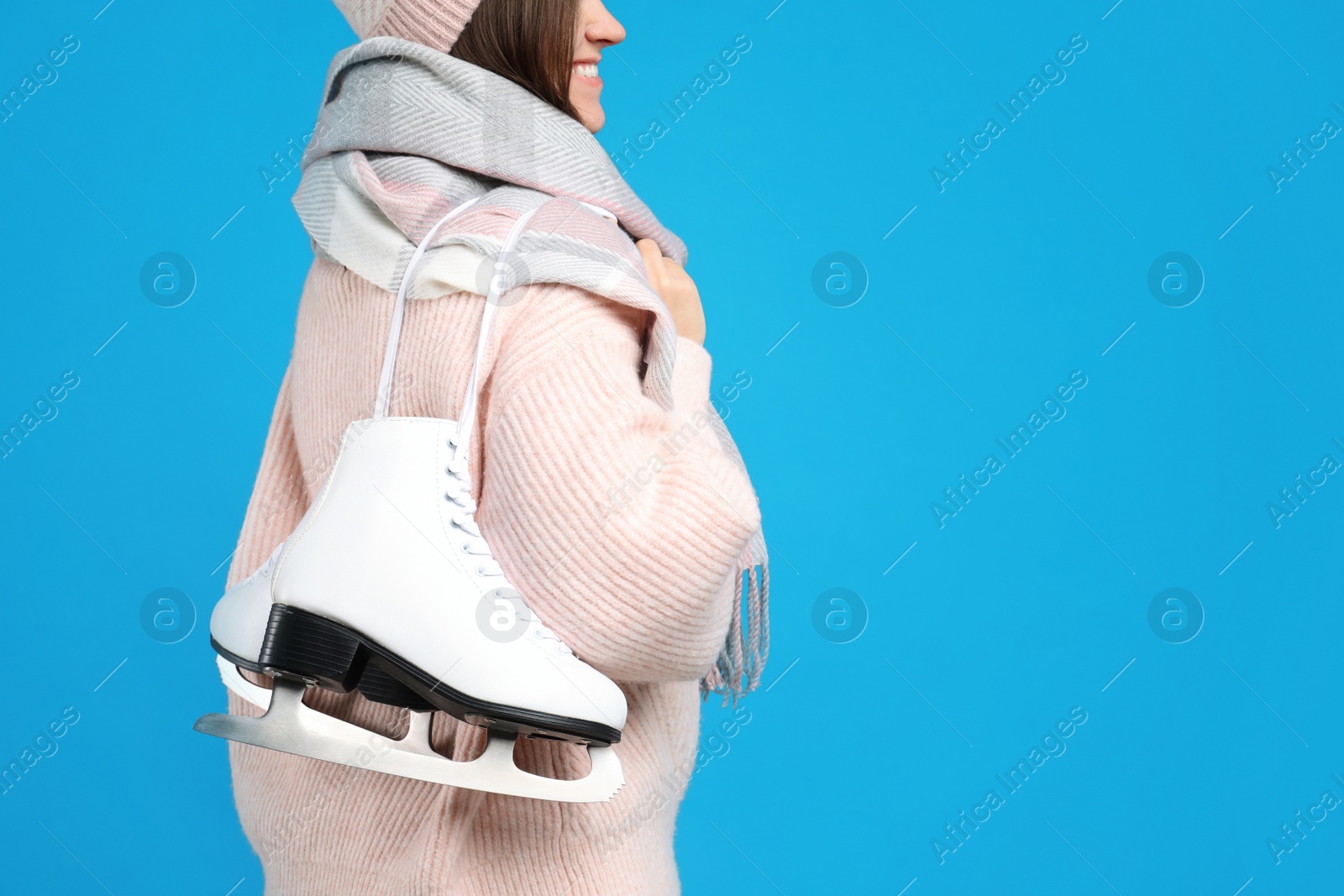 Photo of Happy woman with ice skates on light blue background, closeup. Space for text