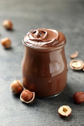 Glass jar with tasty chocolate hazelnut spread and nuts on grey table