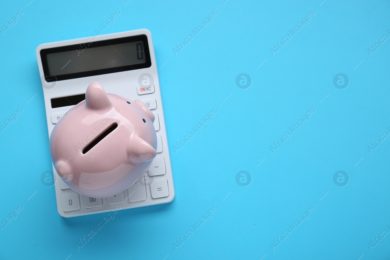 Photo of Piggy bank and calculator on light blue background, top view. Space for text