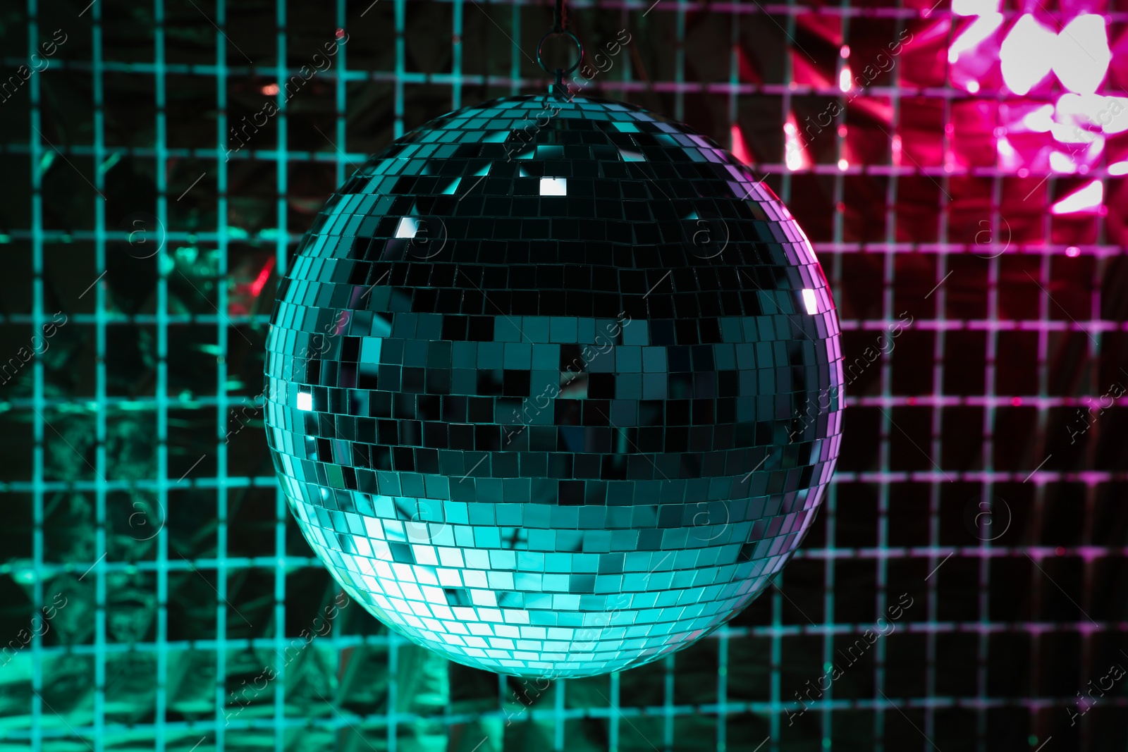 Photo of Shiny disco ball against foil party curtain under turquoise and pink light