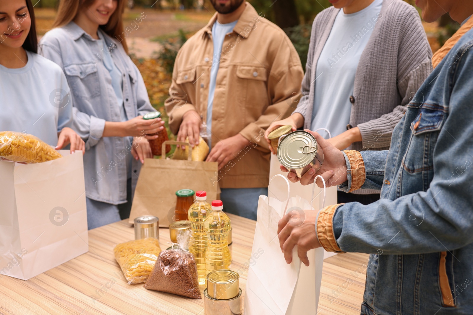 Photo of Group of volunteers packing food products at table outdoors, closeup