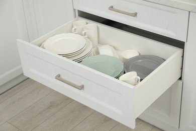 Photo of Clean plates, cups and bowl in drawer indoors