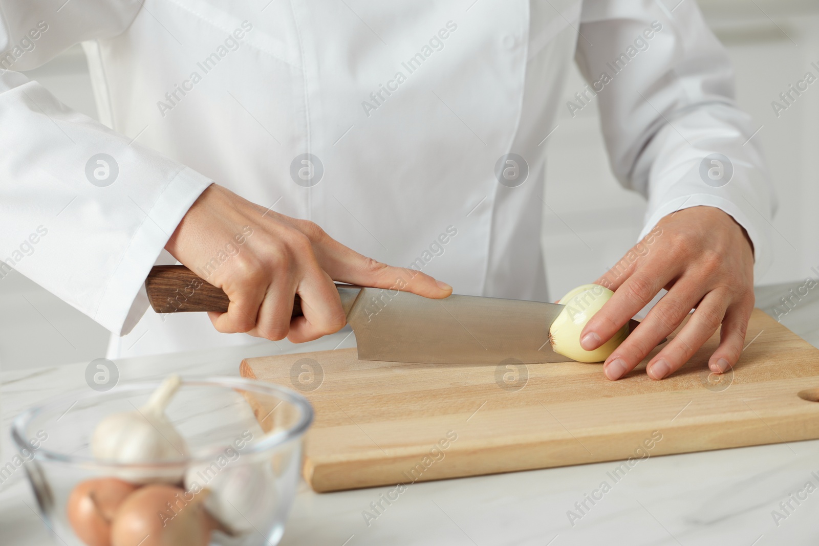 Photo of Professional chef cutting onion at white marble table indoors, closeup