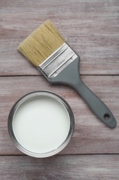 Can of white paint and brush on wooden table, flat lay