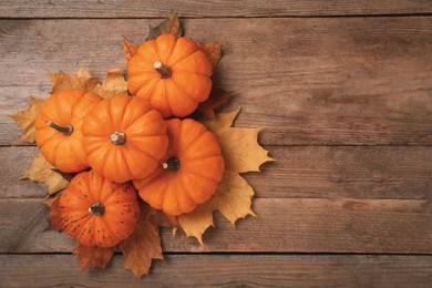 Pile of ripe pumpkins and dry leaves on wooden table, flat lay. Space for text