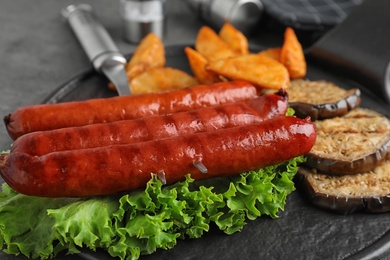 Photo of Delicious grilled sausages and vegetables on grey table, closeup