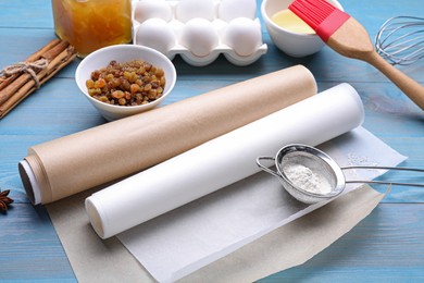 Rolls of baking parchment paper, different ingredients and kitchen tools on light blue wooden table