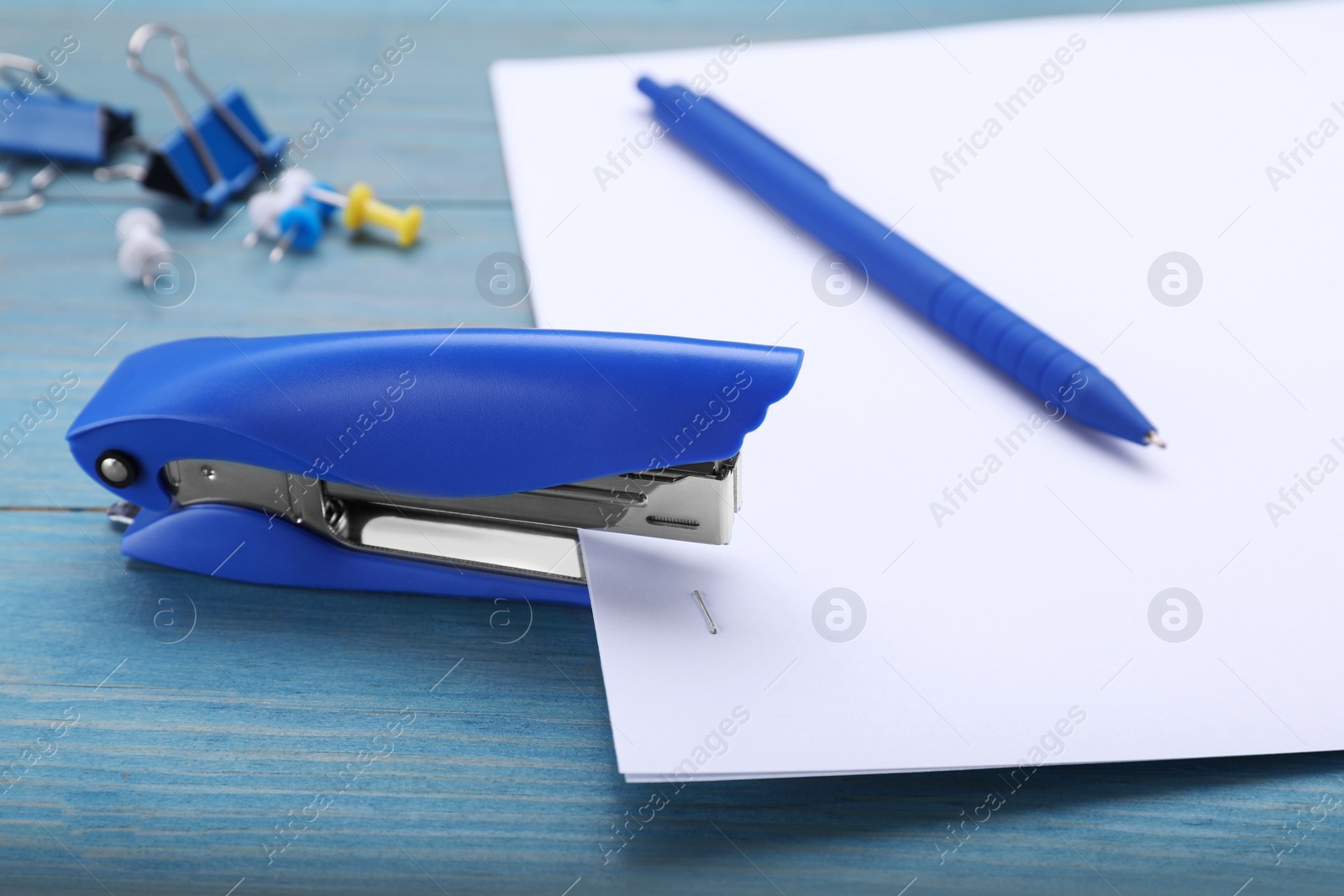 Photo of New bright stapler with paper sheet on light blue wooden table, closeup
