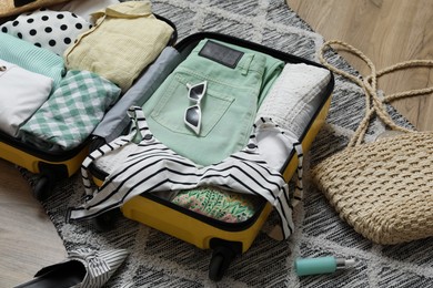 Photo of Open suitcase with summer clothes, accessories and shoes on floor