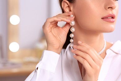 Photo of Young woman trying on elegant pearl earring indoors, closeup. Space for text