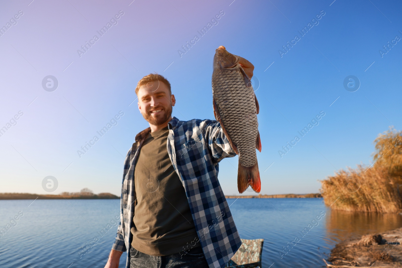 Photo of Fisherman holding caught fish at riverside. Recreational activity