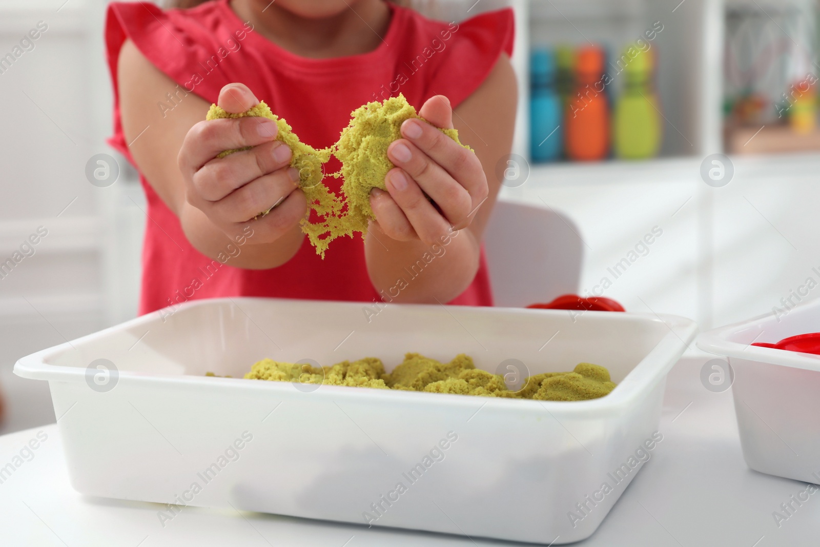 Photo of Little girl playing with bright kinetic sand at table indoors, closeup