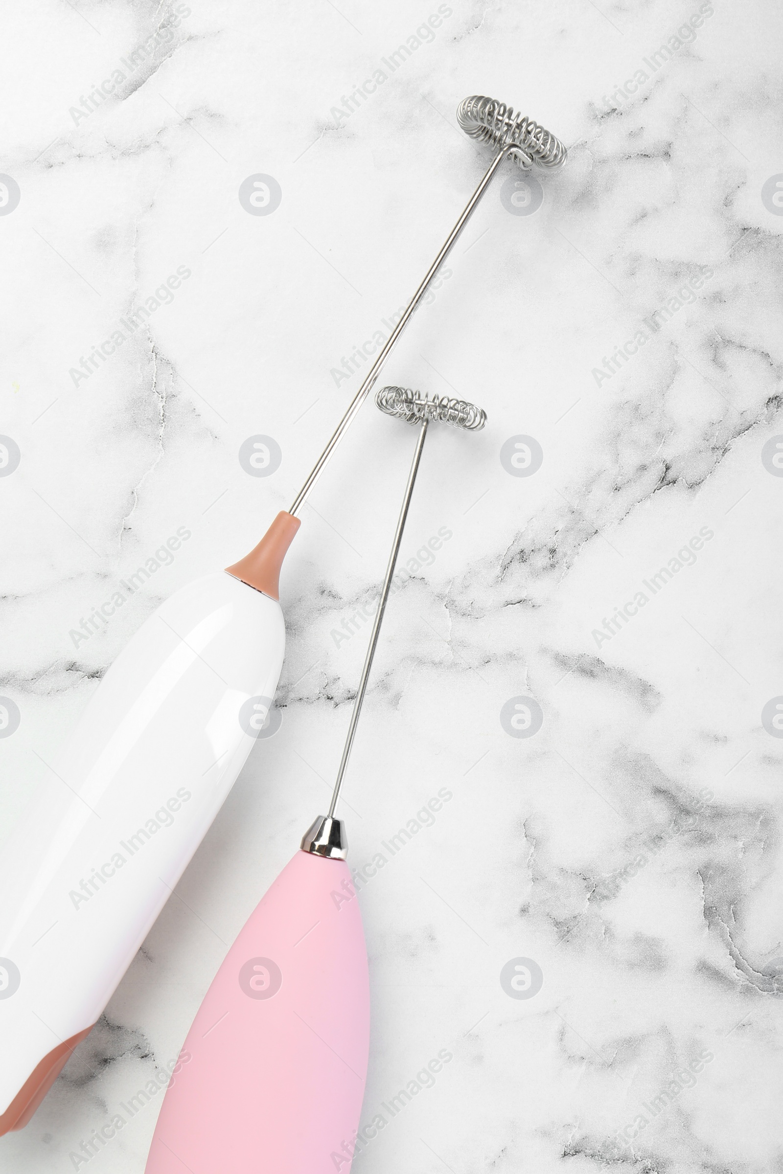 Photo of Pink milk frother wands on white marble table, top view