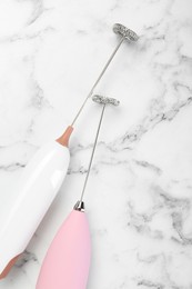 Pink milk frother wands on white marble table, top view