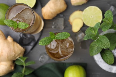 Photo of Glasses of tasty ginger ale with ice cubes and ingredients on grey wooden table, flat lay