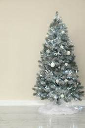 Photo of Decorated Christmas tree with white faux fur skirt near beige wall. Space for text