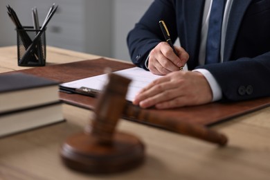 Photo of Notary writing notes at wooden table in office, closeup