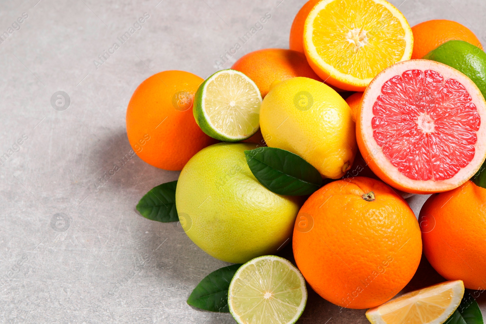 Photo of Pile of different fresh citrus fruits and leaves on grey textured table, closeup. Space for text