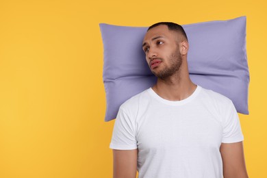 Photo of Tired man with pillow on orange background, space for text. Insomnia problem