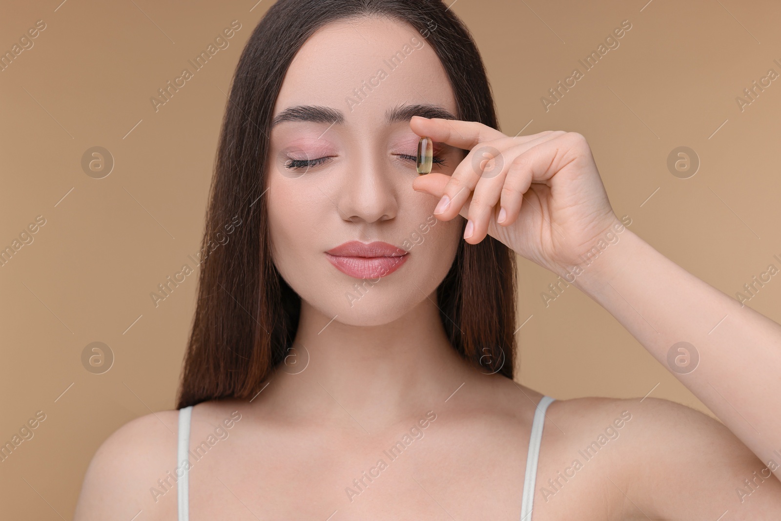 Photo of Beautiful young woman with vitamin pill on beige background