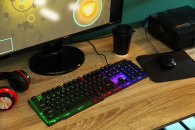 Photo of Modern RGB keyboard, computer and headphones on wooden table indoors