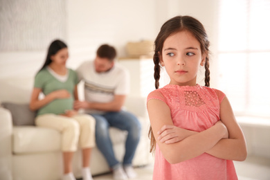 Photo of Unhappy little girl and her father with pregnant mother at home. Feeling jealous towards unborn sibling