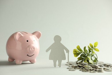 Pension savings. Figure of senior woman, piggy bank, coins and green twigs on grey background