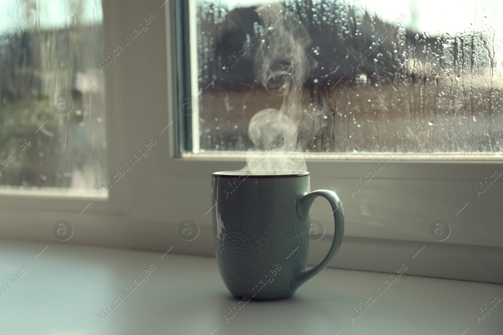 Photo of Cup of hot drink near window on rainy day