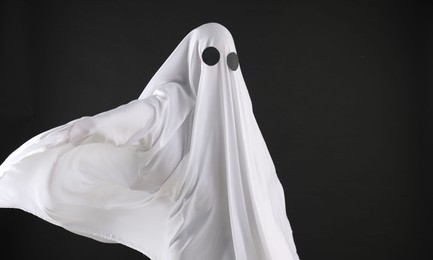 Creepy ghost. Person covered with sheet on black background, space for text