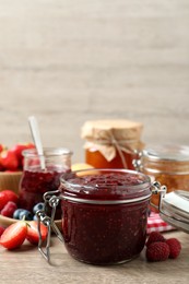 Photo of Jars with different jams and fresh berries on wooden table