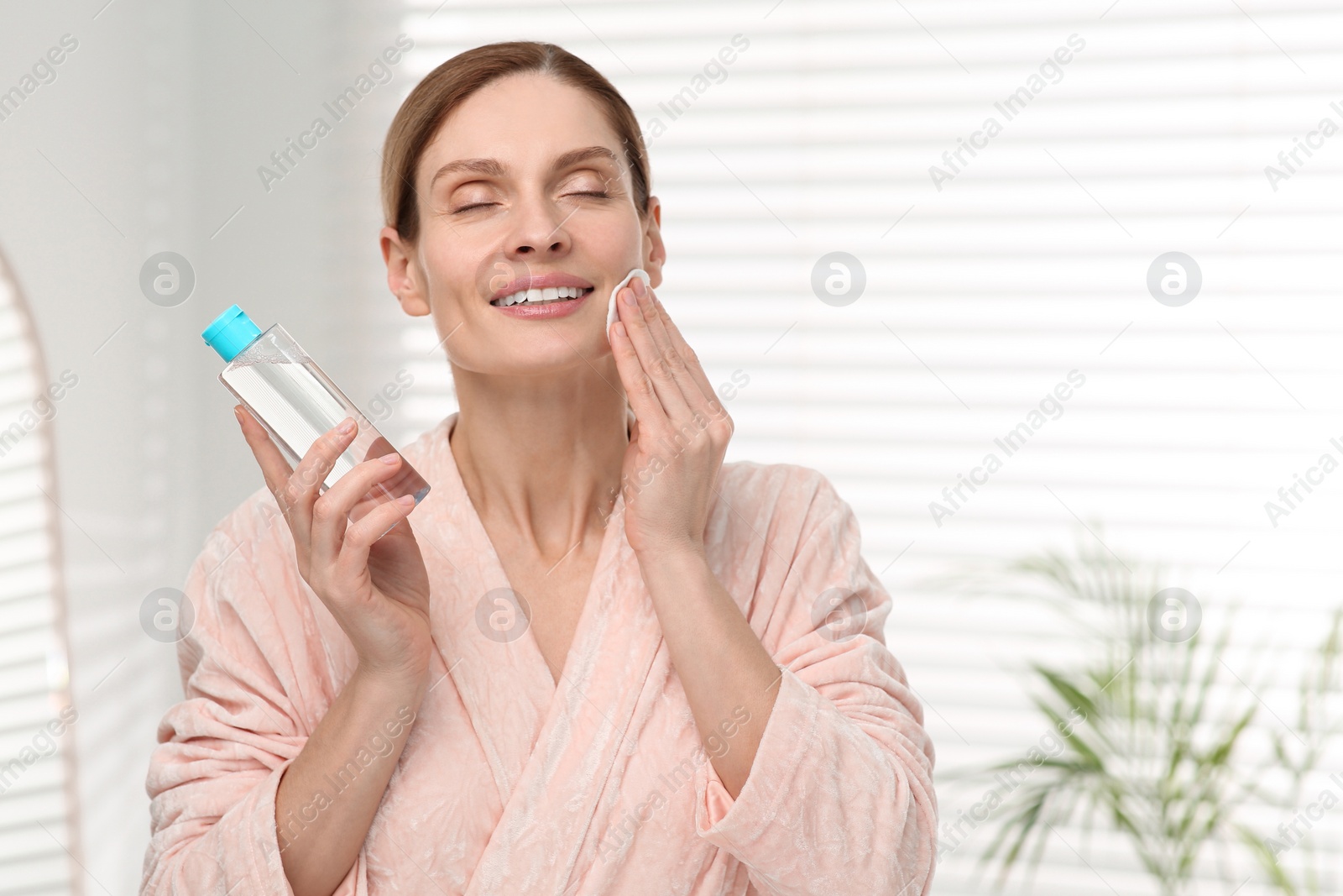 Photo of Beautiful woman removing makeup with cotton pad indoors