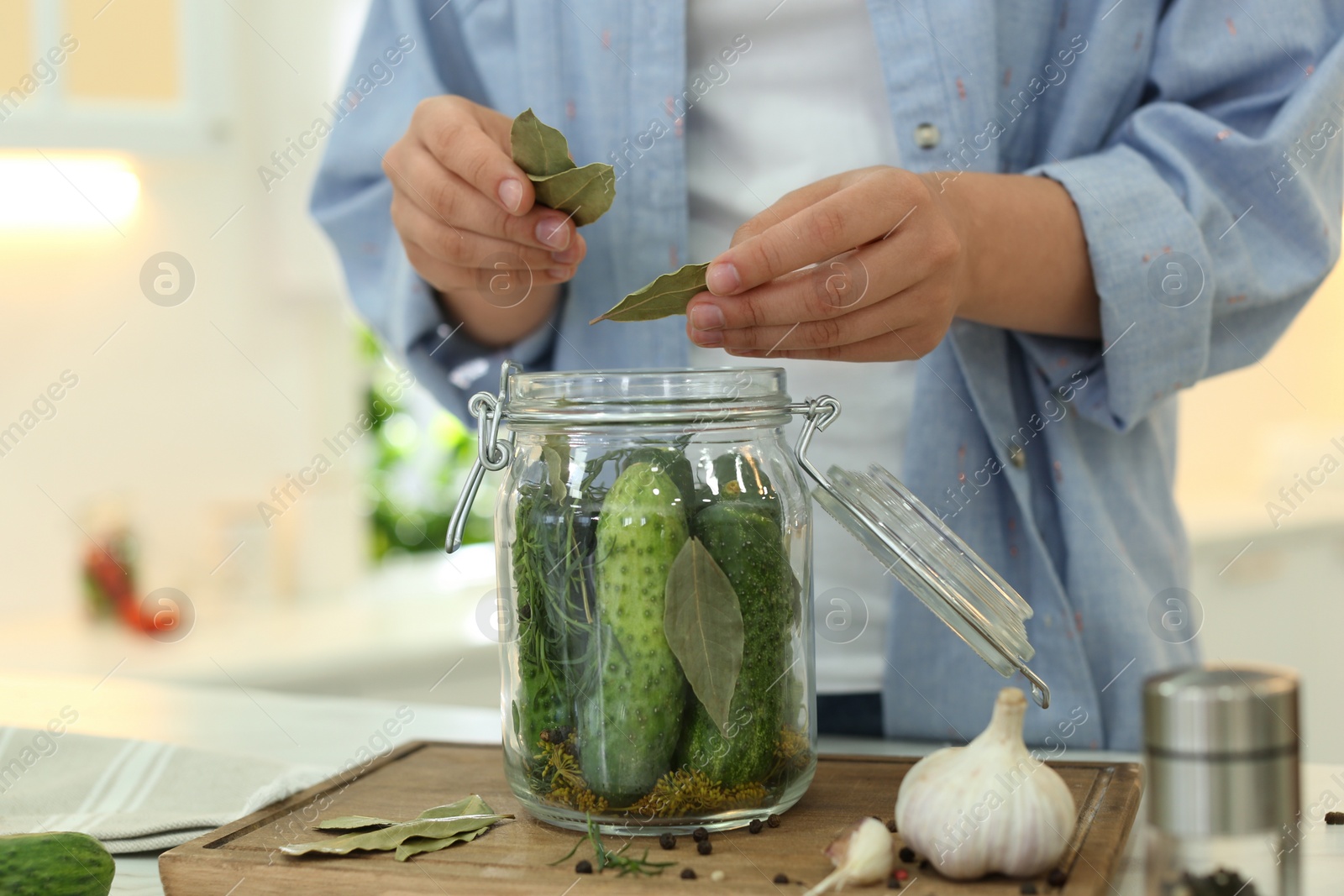 Photo of Woman putting bay leaves into pickling jar at table in kitchen, closeup