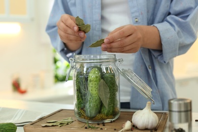 Woman putting bay leaves into pickling jar at table in kitchen, closeup