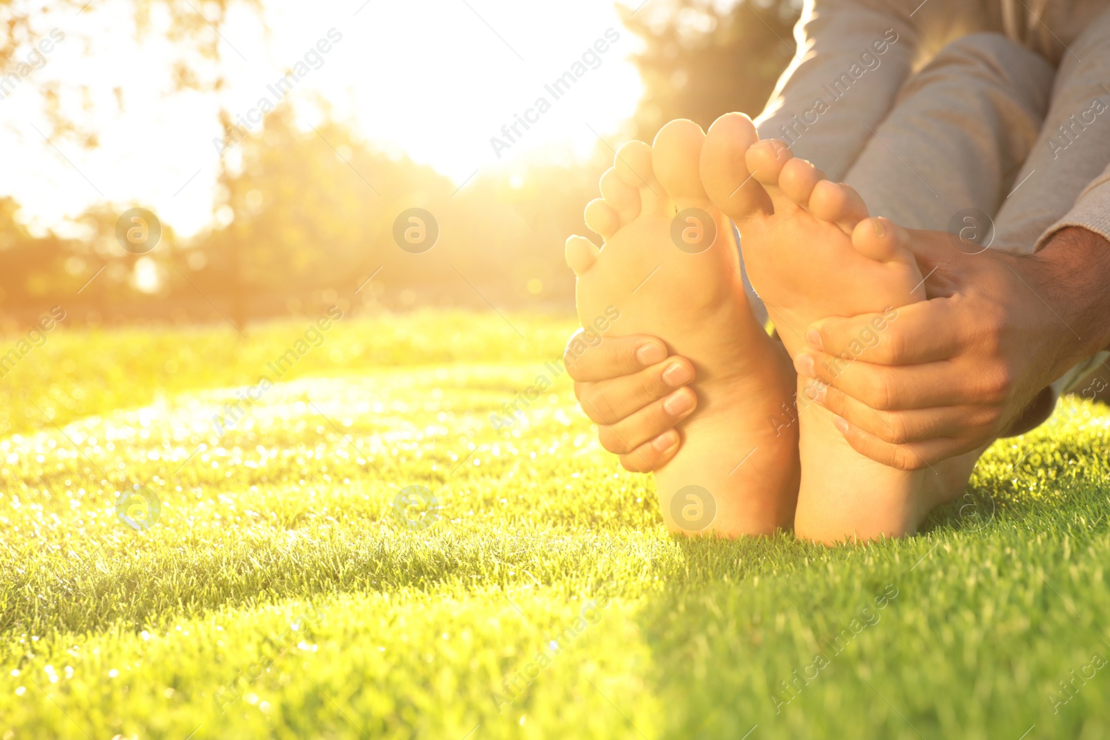 Photo of Man sitting barefoot on fresh green grass outdoors, closeup