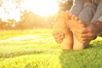 Photo of Man sitting barefoot on fresh green grass outdoors, closeup