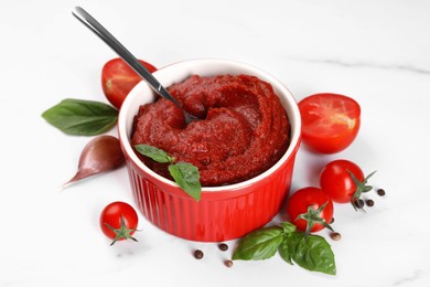 Tasty tomato paste in bowl and ingredients on white table