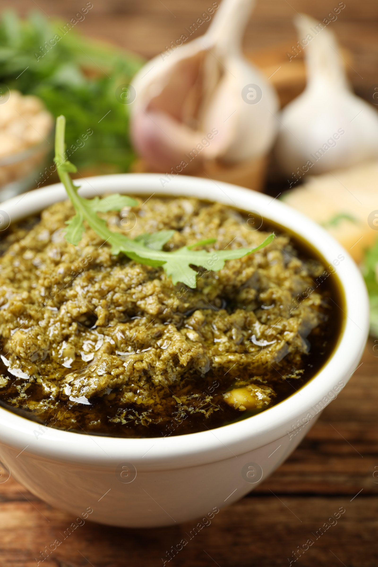 Photo of Bowl of tasty arugula pesto on wooden table, closeup