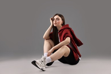 Beautiful woman in sportswear sitting on grey background