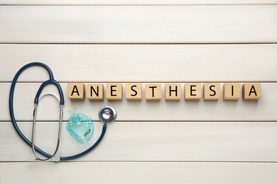 Photo of Word Anesthesia made of wooden cubes, stethoscope and mask on white table, flat lay