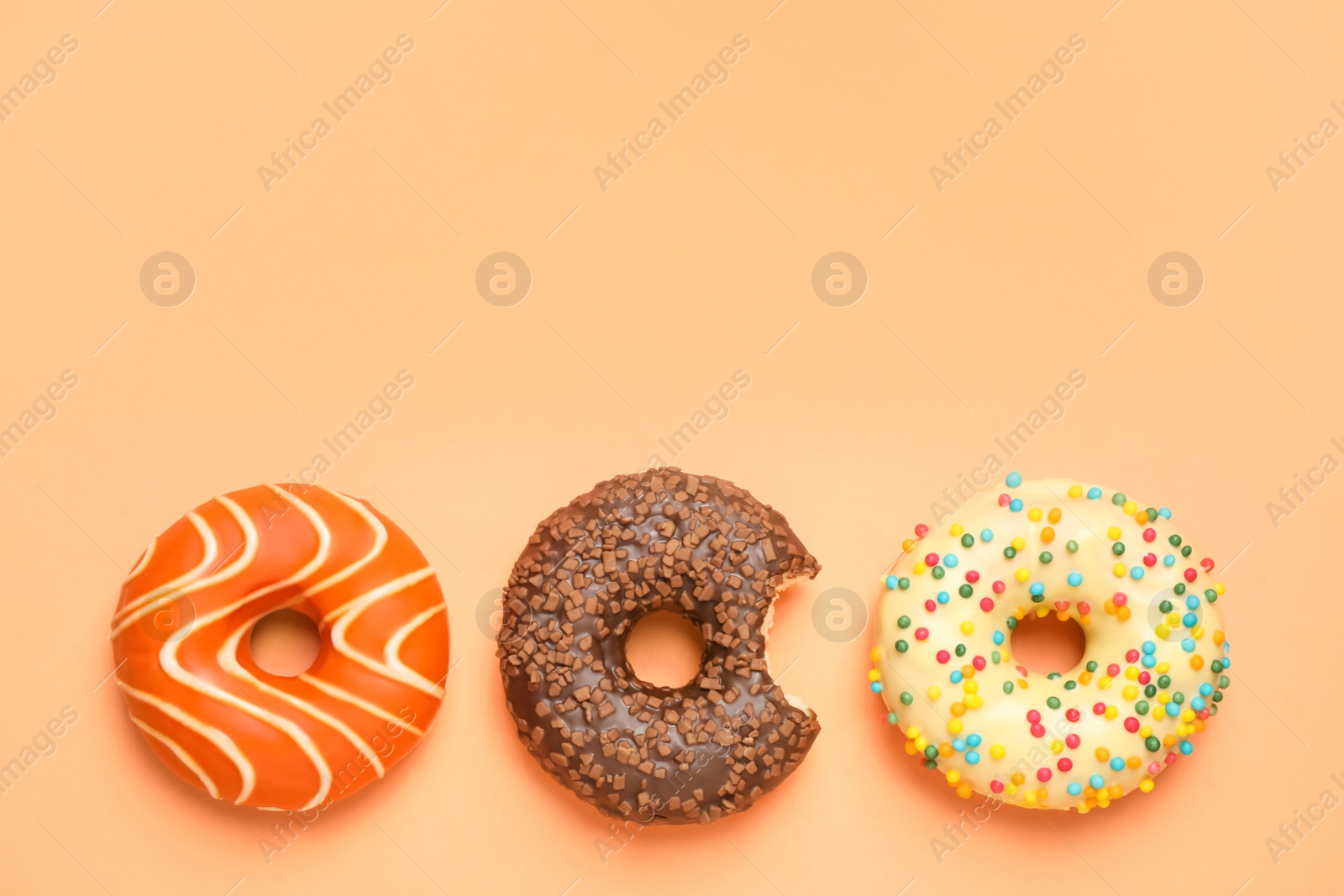 Photo of Delicious glazed donuts on orange background, flat lay. Space for text