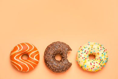 Photo of Delicious glazed donuts on orange background, flat lay. Space for text