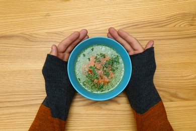 Photo of Man with bowl of soup at wooden table, top view. Flu treatment