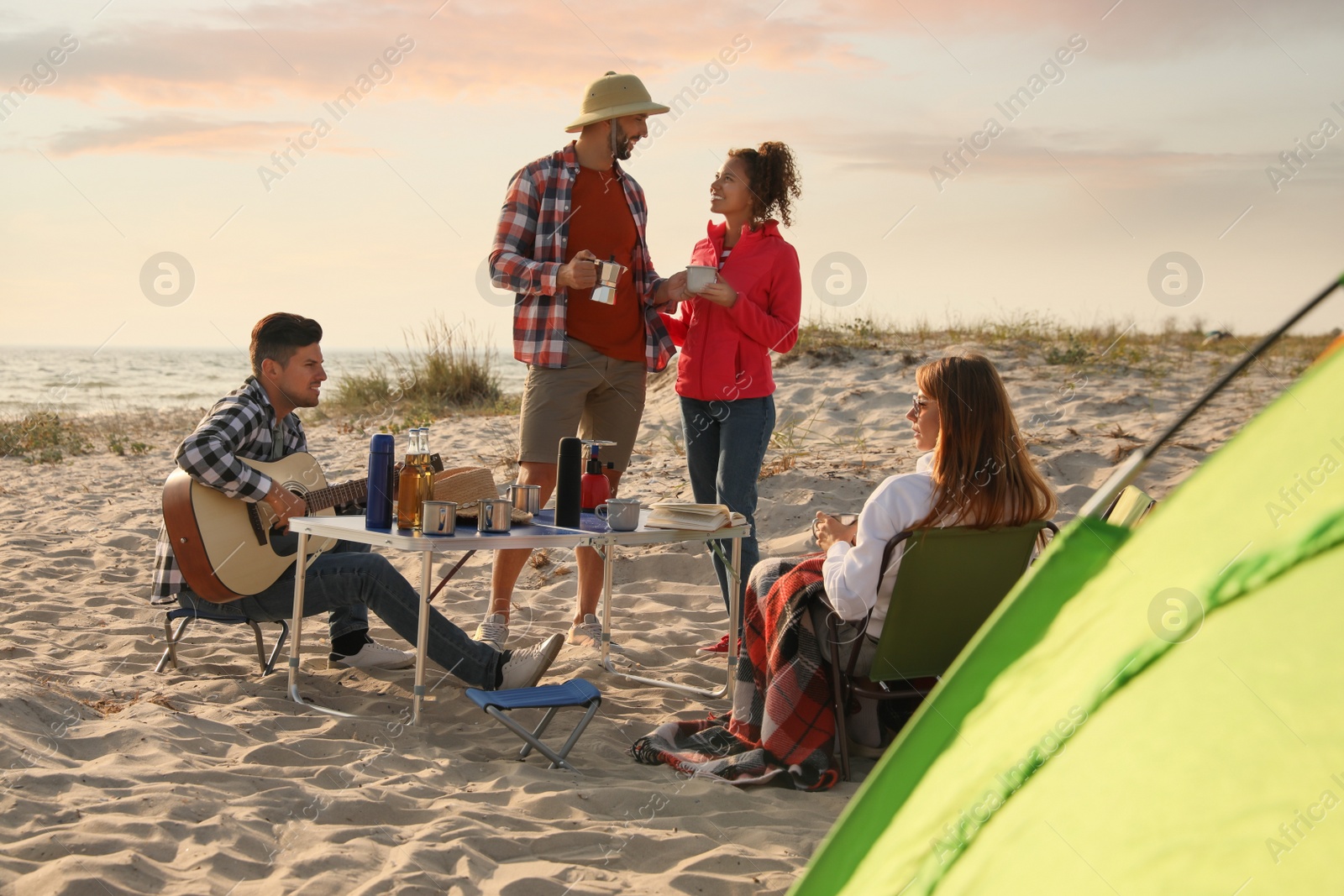 Photo of Friends resting near camping tent on sandy beach